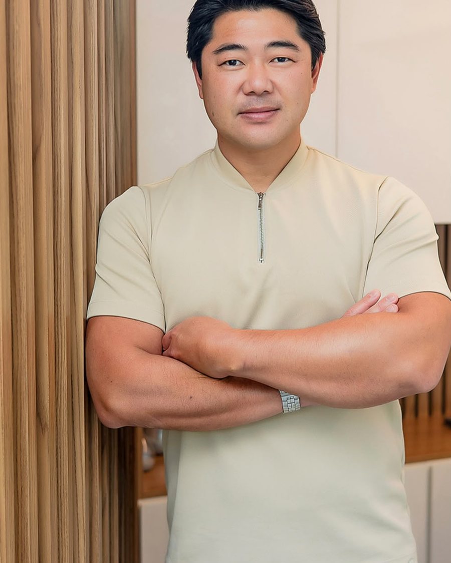 Dr. Rafael Kenji de pé no consultório, de braços cruzados